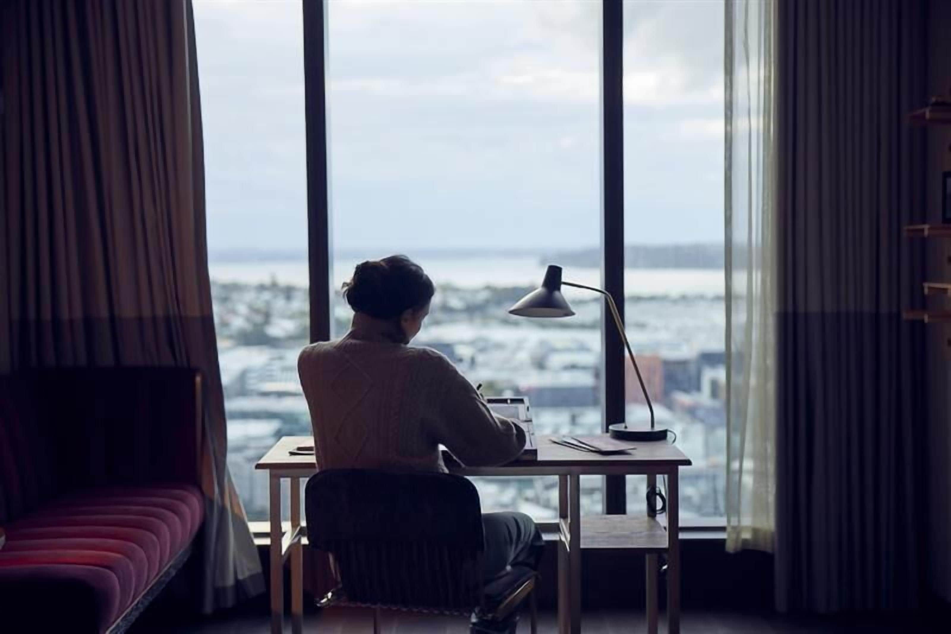 A person sitting at a desk by a large window overlooking a cityscape.