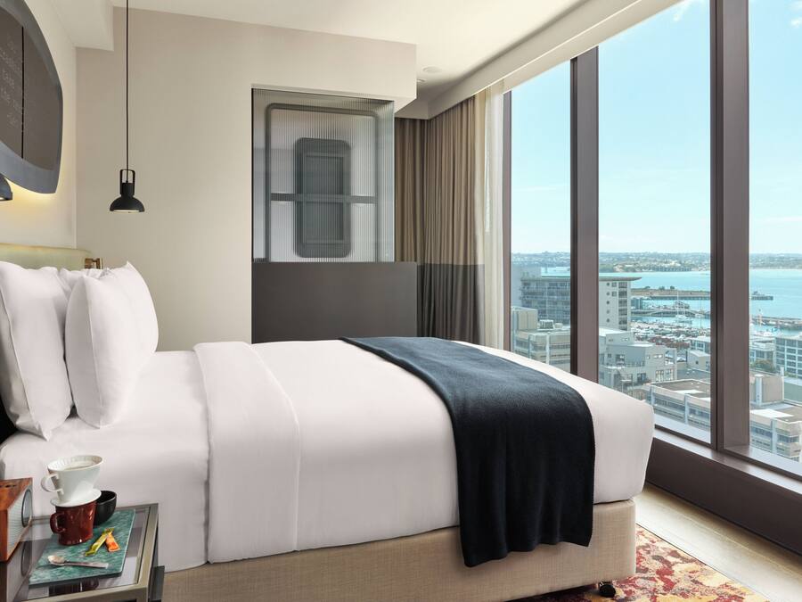 Une chambre d’hôtel moderne avec un grand lit, une vue sur la ville, un bureau avec une tasse à café et une fenêtre avec des rideaux.