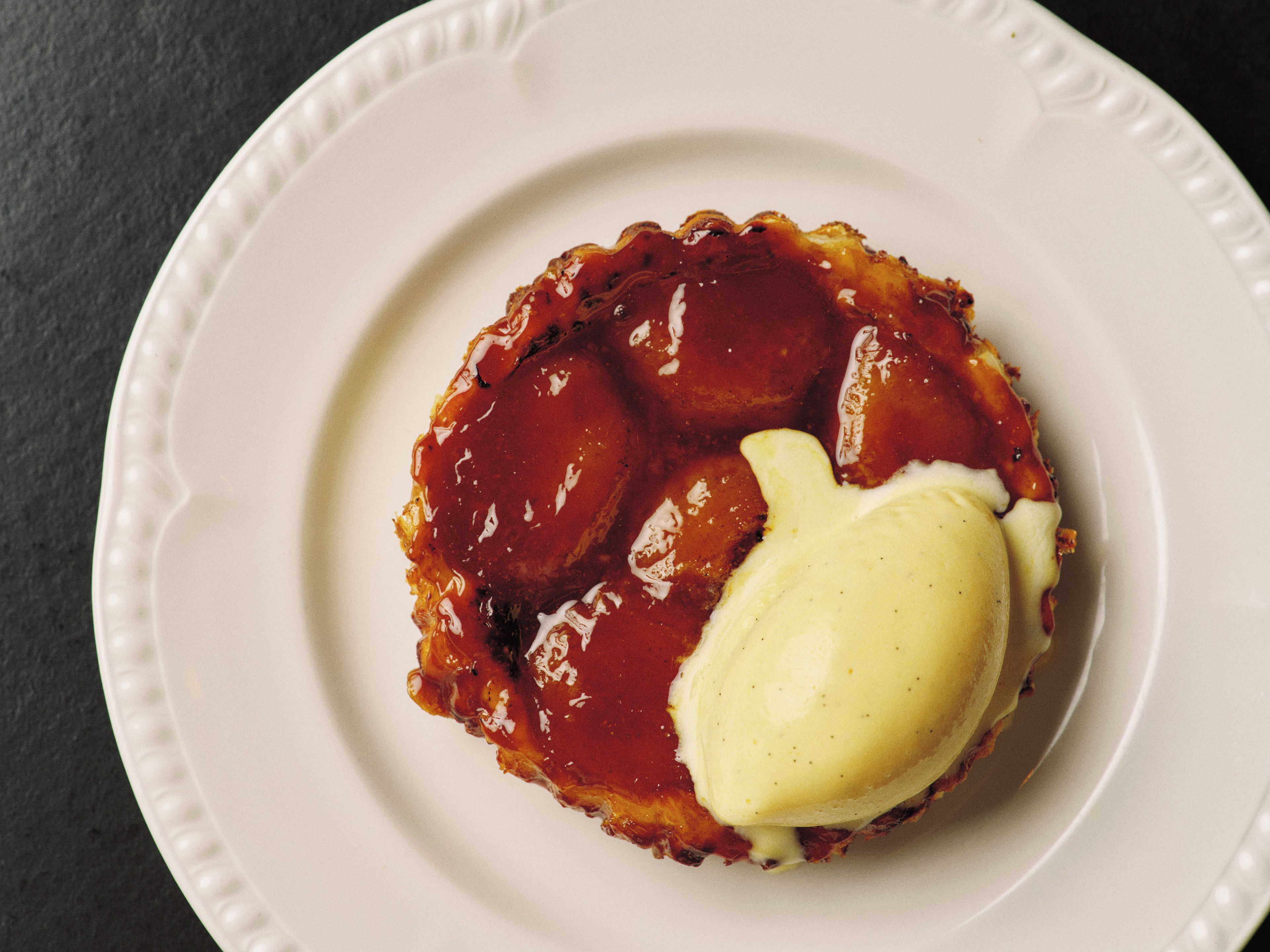 Un dessert servi dans une assiette blanche, surmonté d’un glaçage brillant et d’une quenelle de crème.