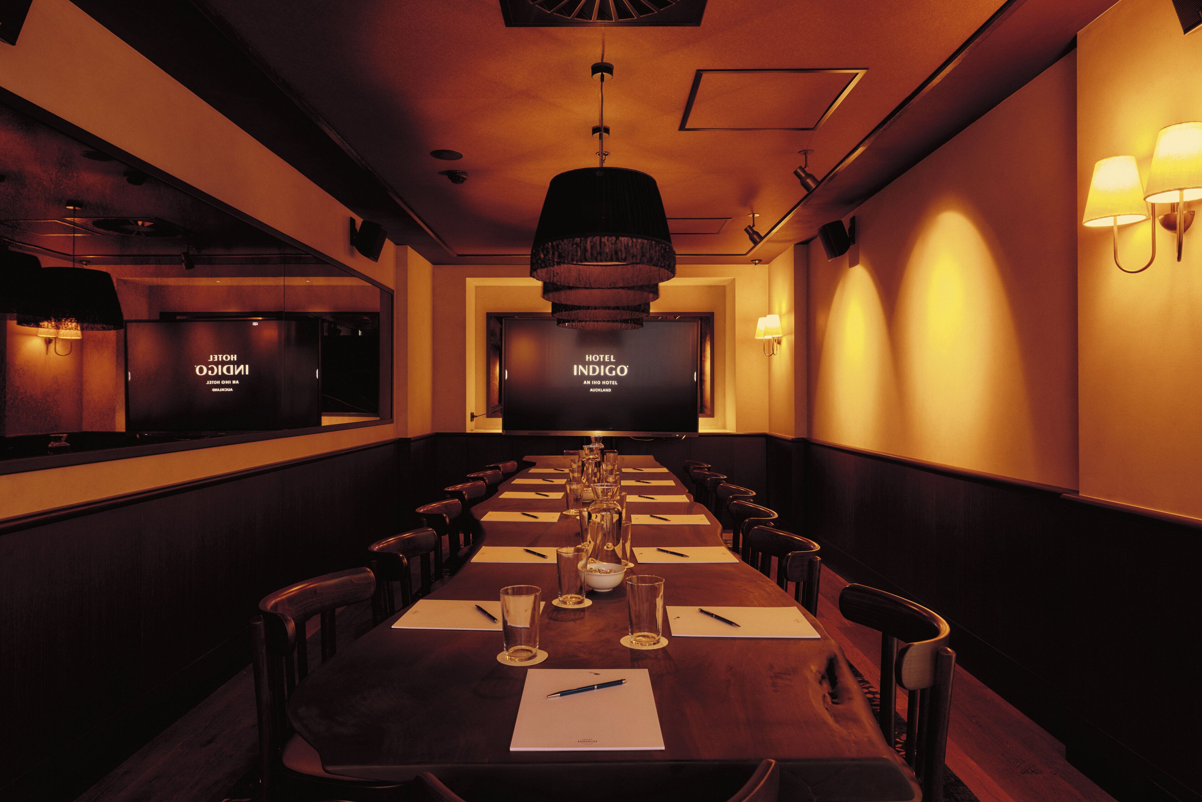 A conference room with a long table, chairs, a projector screen, and a television.
