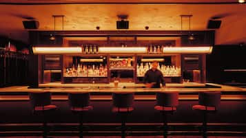 A bar area with a long counter, multiple shelves of bottles, and four stools.