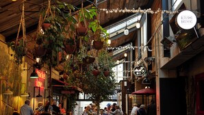 An indoor dining area with hanging plants, wooden tables, and chairs. There are people dining and a neon sign in the background. - Hotel Indigo Auckland by IHG (Auckland)