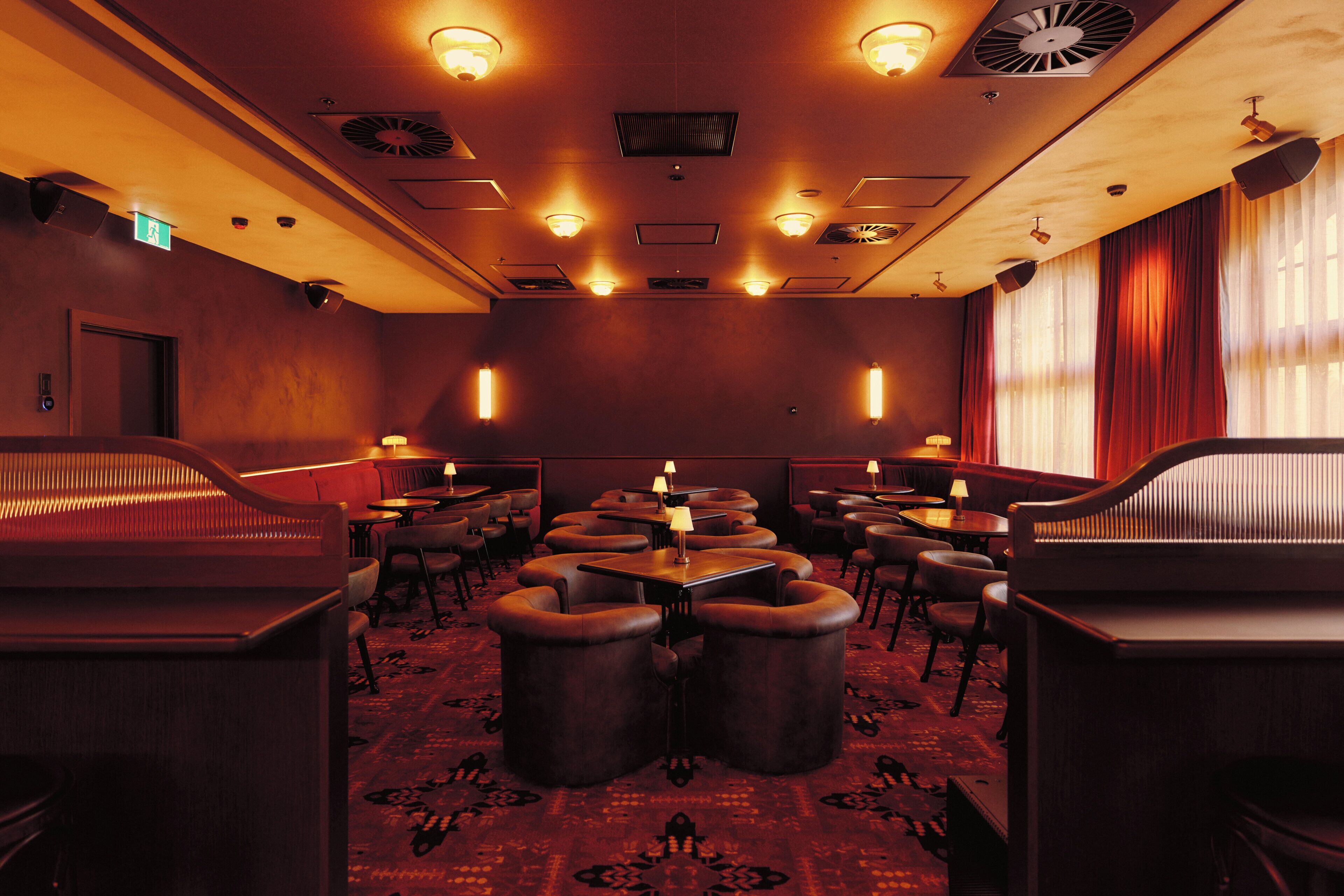 A dimly lit restaurant with booths and tables, patterned carpet, and ceiling vents.
