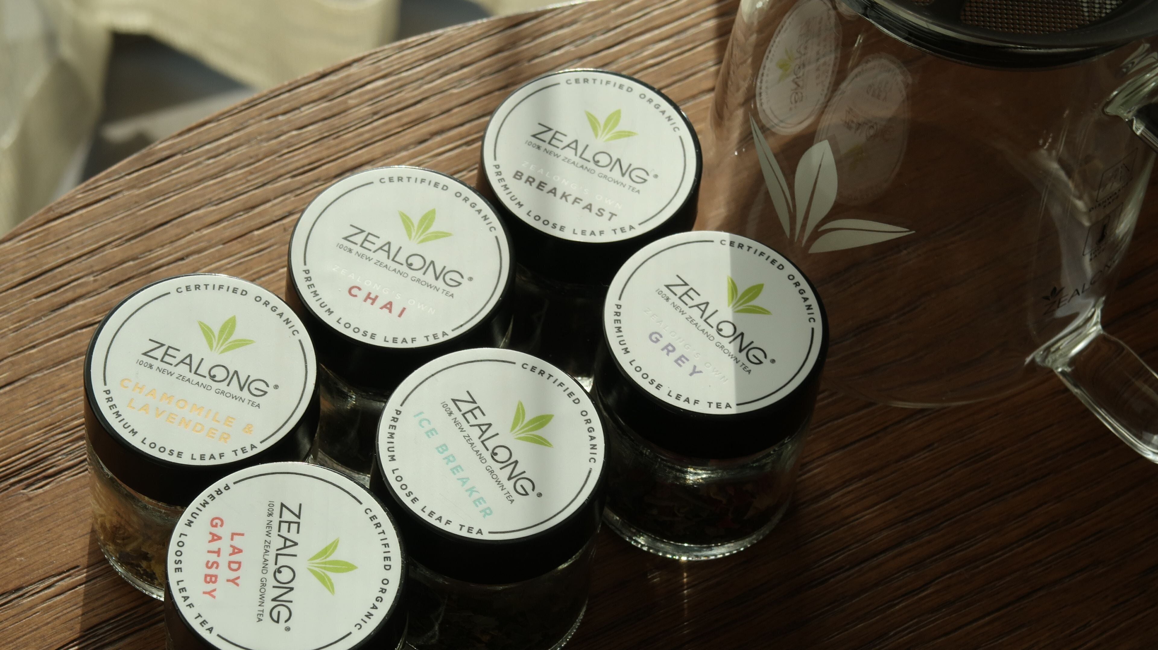 Seis latas de té con la etiqueta 'Zealong' sobre una superficie de madera.