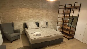 Une chambre à coucher comprenant un lit, une chaise, une petite table, un tapis rond, un luminaire suspendu et un mur en bois.
