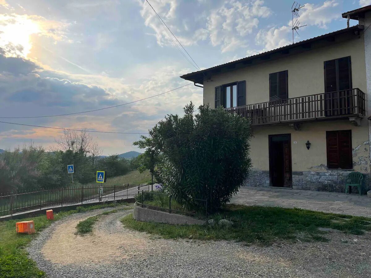 Un edificio a due piani con un balcone, un vialetto sterrato e un sentiero recintato.