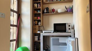 A compact kitchen with a microwave, a small refrigerator, and a wooden cabinet with various kitchen items.