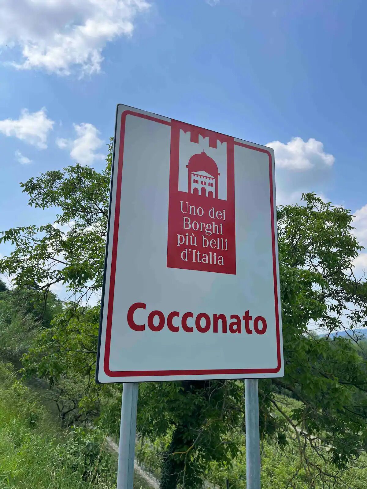 A sign with the text "Cocconato" and a symbol of a building with a dome, indicating a historical or cultural site.