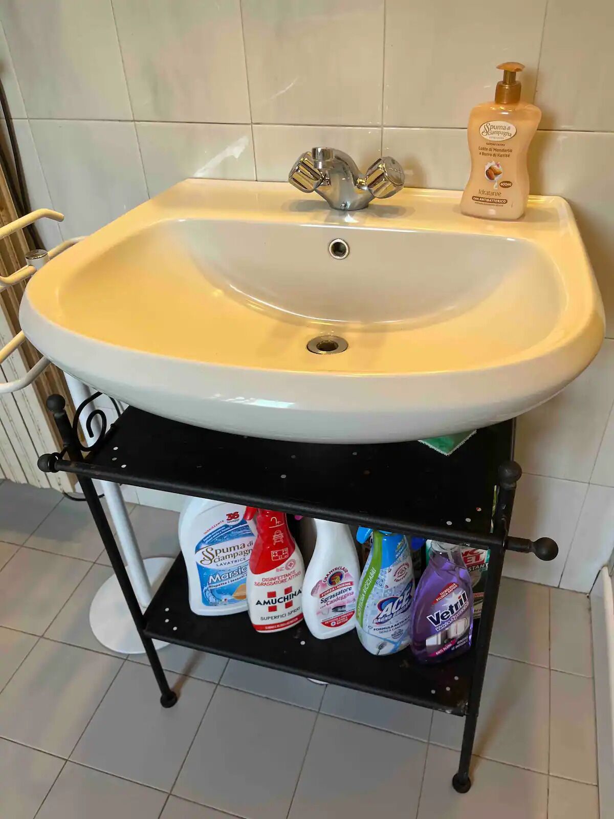 Un lavabo de baño con un estante negro debajo que contiene diversos productos de limpieza.