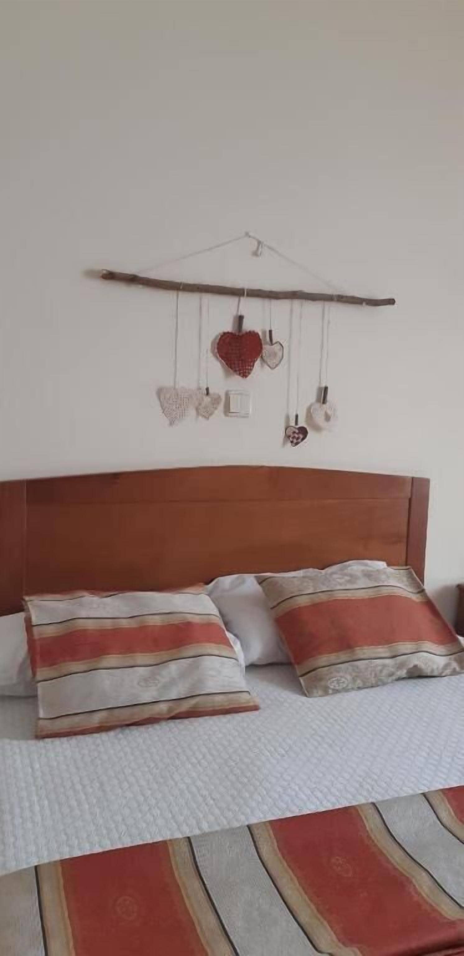 A bed with two pillows, a wooden headboard, and a wall-mounted heart decoration.