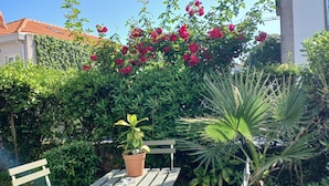 A patio with a table and two chairs, surrounded by lush greenery and flowering plants.