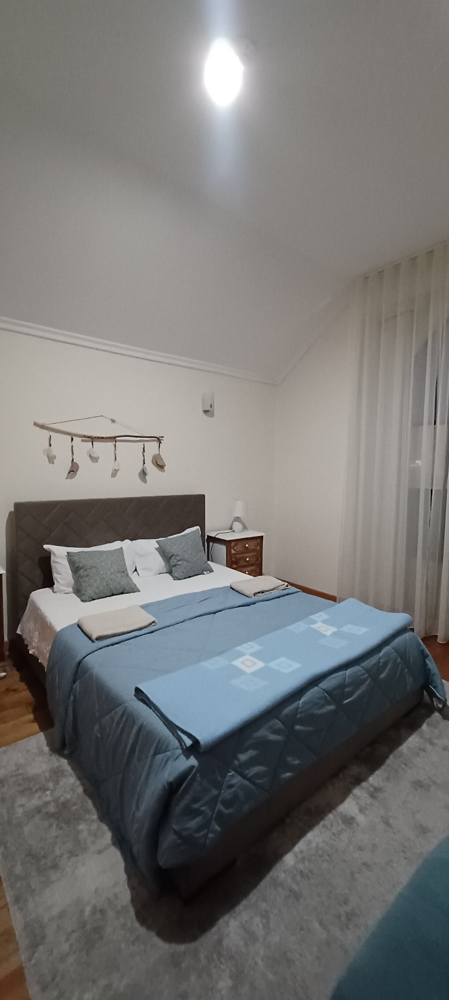 Une chambre à coucher comprenant un lit, une table de chevet, une étagère fixée au mur et une fenêtre avec des rideaux.
