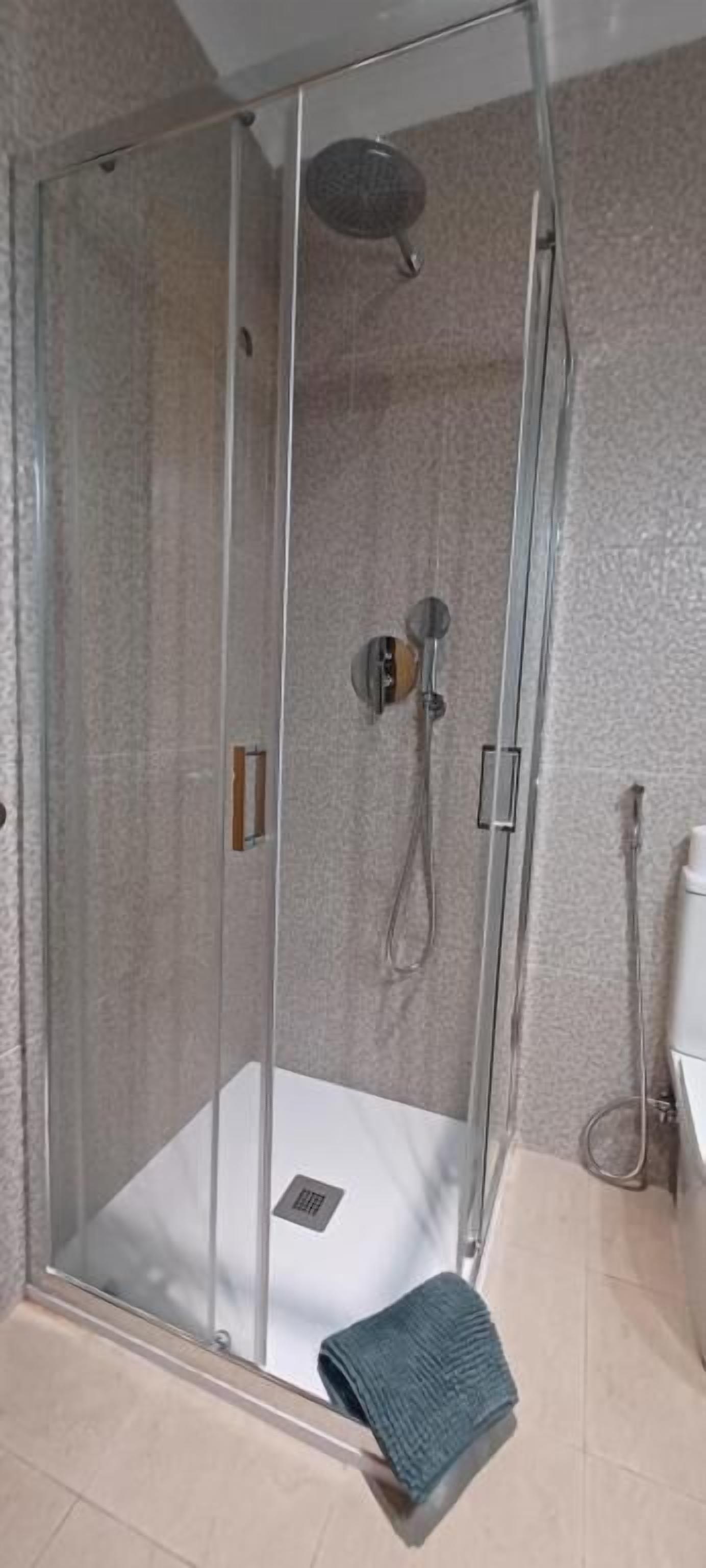A glass-enclosed shower stall with a handheld showerhead and a wall-mounted faucet.