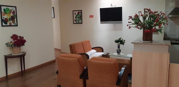 Habitación de hotel con una cama, dos sillones naranjas, una mesita, un televisor y un jarrón con flores.