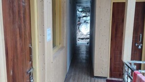 Un estrecho pasillo con paredes y puertas de madera, que conduce a una ventana con vistas a rocas y árboles.
