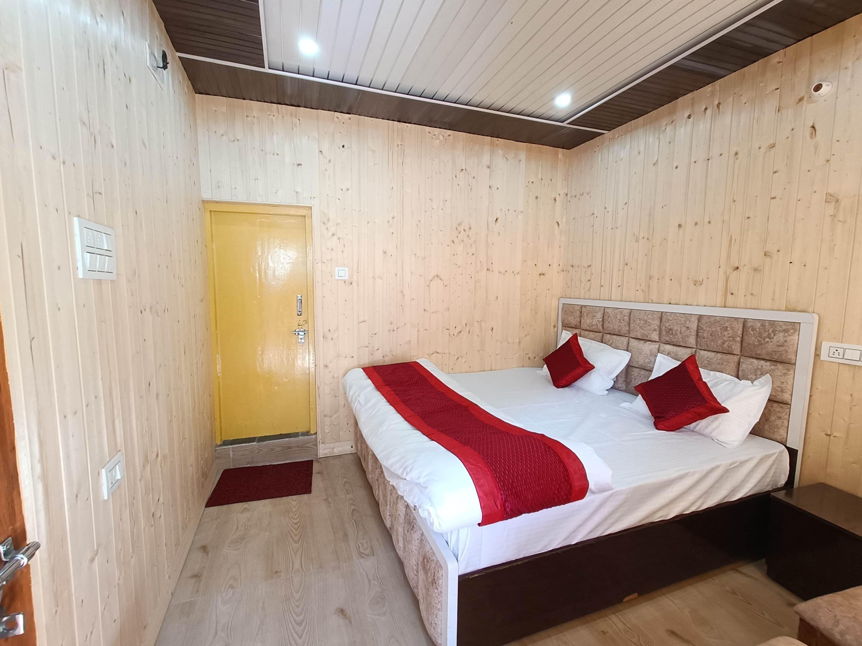 A wooden-paneled room with a bed, a yellow door, and a red carpet.