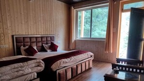 Habitación con dos camas, un banco, una ventana que da a árboles y suelo de madera.
