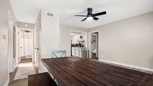 A spacious dining area with a wooden table and benches, a ceiling fan, and a view into the kitchen.