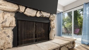 A stone fireplace with a black screen, a stone ledge, and a view of a deck with chairs.