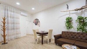 Un salon moderne avec un canapé en cuir marron, une table basse en bois sur laquelle sont posés des magazines, une table à manger avec des chaises et un ventilateur décoratif fixé au mur.