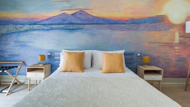 Une chambre à coucher avec un lit, deux tables de chevet et un tableau représentant un coucher de soleil sur des montagnes.