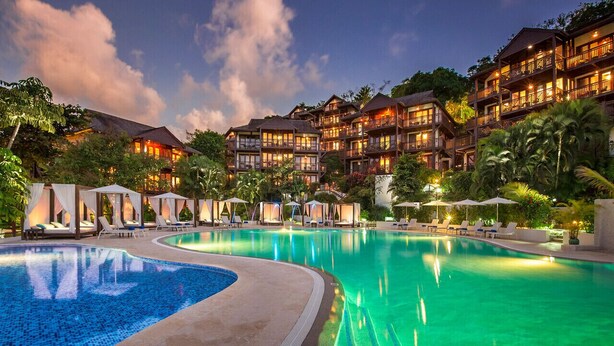 A resort with a large swimming pool, multiple guest rooms, and lush tropical landscaping.
