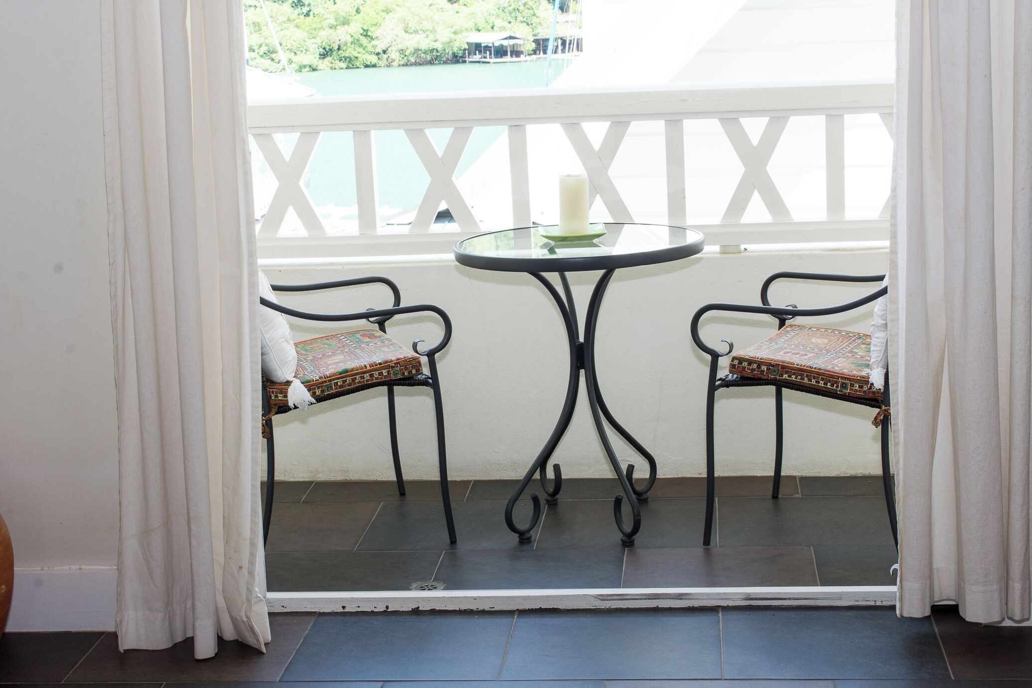 Un balcone con due sedie e un tavolo, una ringhiera bianca e vista su un corpo d'acqua.