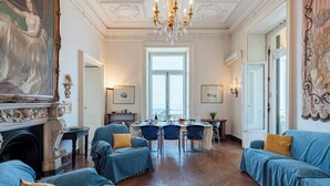 Une pièce avec une cheminée, des canapés bleus, une table à manger dressée pour quatre personnes et une grande fenêtre.
