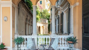Un espace extérieur abrité, aménagé avec deux chaises et une table, entouré de colonnes et doté d’un sol à carreaux.