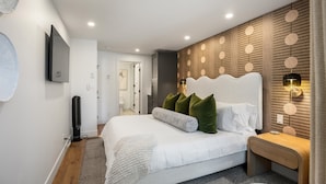 A modern bedroom with a large bed, a bedside table, a wall-mounted TV, and a patterned wall.