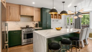 A modern kitchen with green cabinets, a marble island, and a gas stove.