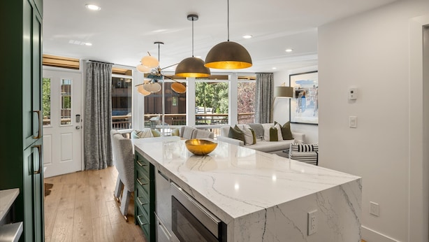 A modern kitchen with a marble island, pendant lighting, and a view to the outdoors.