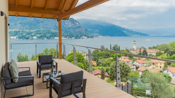 A balcony with a wooden ceiling, furnished with two chairs and a small table, overlooking a lake with mountains in the background. - Villa Cosima in Bellagio With Private Pool (Bellagio)