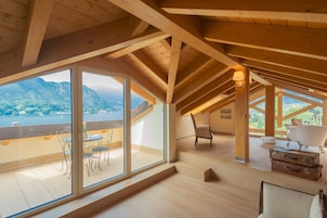 Um quarto espaçoso com grandes janelas que oferecem vista para as montanhas, vigas de madeira no teto e uma área de estar acolhedora com banheira e malas.