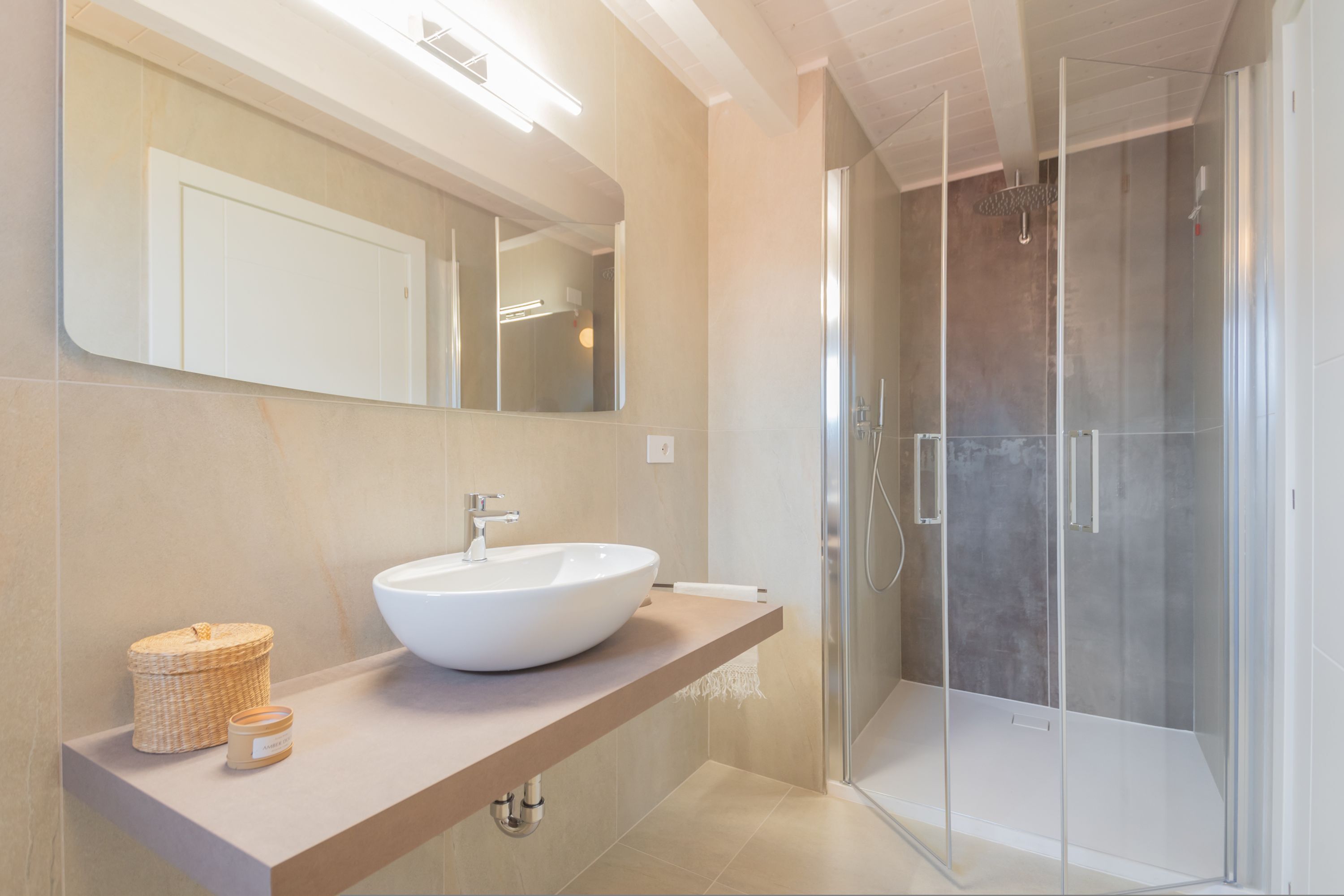 Une salle de bain moderne avec un grand miroir, un lavabo blanc, une cabine de douche et un plan de toilette beige.