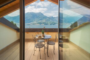 A balcony with a table and chairs, overlooking a lake and mountains.