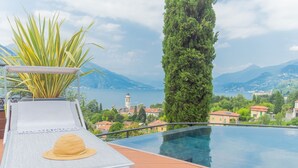 A infinity pool with a view of a mountainous landscape and a distant tower. - Villa Cosima in Bellagio With Private Pool (Bellagio)