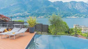 An infinity pool with a wooden deck, lounge chairs, and a potted plant. - Villa Cosima in Bellagio With Private Pool (Bellagio)