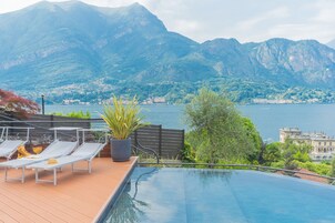 An infinity pool with a wooden deck, lounge chairs, and a potted plant.
