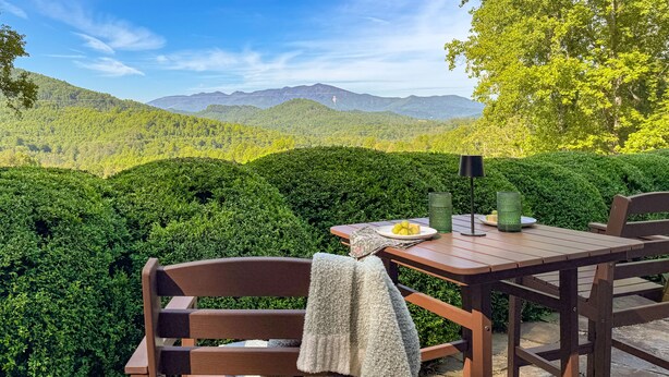 A table with a plate of lemons and a candle, set against a backdrop of lush green hills and a clear blue sky.