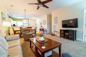 A living room with a sofa, armchair, coffee table, TV, and a dining area with chairs and a table.