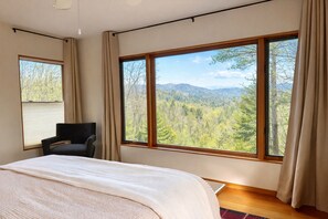 Une chambre à coucher avec un lit, une chaise et de grandes fenêtres donnant sur la forêt.