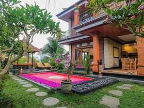 A two-story house with a balcony, a garden with a colorful flower bed, and a dining area with a table and chairs.