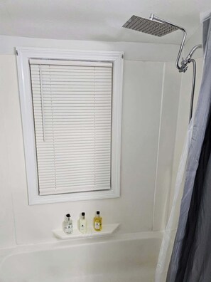 A bathroom with a shower, a window with blinds, and a shelf with toiletries. - Private Apartment  in Berlin (Berlin)