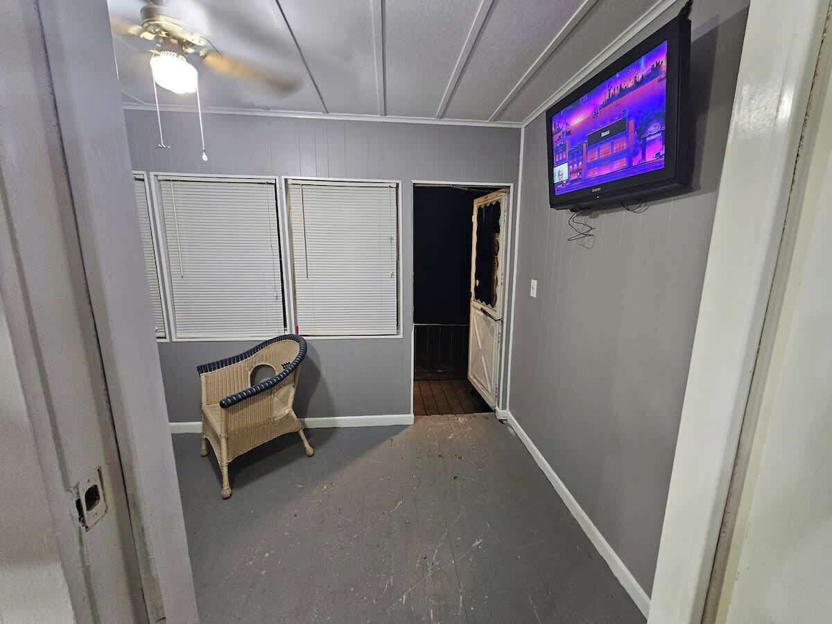 Een kamer met een aan de muur bevestigde televisie, een plafondventilator en een rieten stoel.