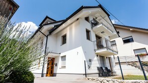 A two-story building with a white facade, a wooden door, and a balcony with a metal railing. - PJ Apartments & Wellness - Hot Tub & Sauna - Free Parking (Cerklje na Gorenjskem)