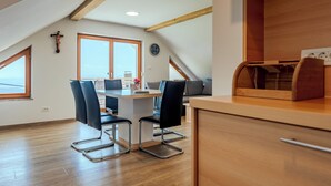 A modern kitchen with wooden beams, a dining area with a table and chairs, and a large window offering a view. - PJ Apartments & Wellness - Hot Tub & Sauna - Free Parking (Cerklje na Gorenjskem)