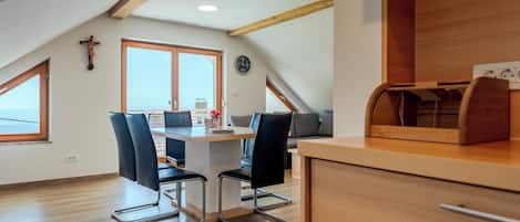 A modern kitchen with wooden beams, a dining area with a table and chairs, and a large window offering a view.