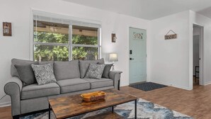 A living room with a grey sofa, a wooden coffee table, a lamp, and a door with a sign.