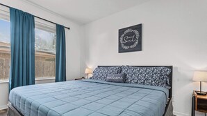 A bedroom with a bed, a nightstand, a wall-mounted picture, and a window with curtains.